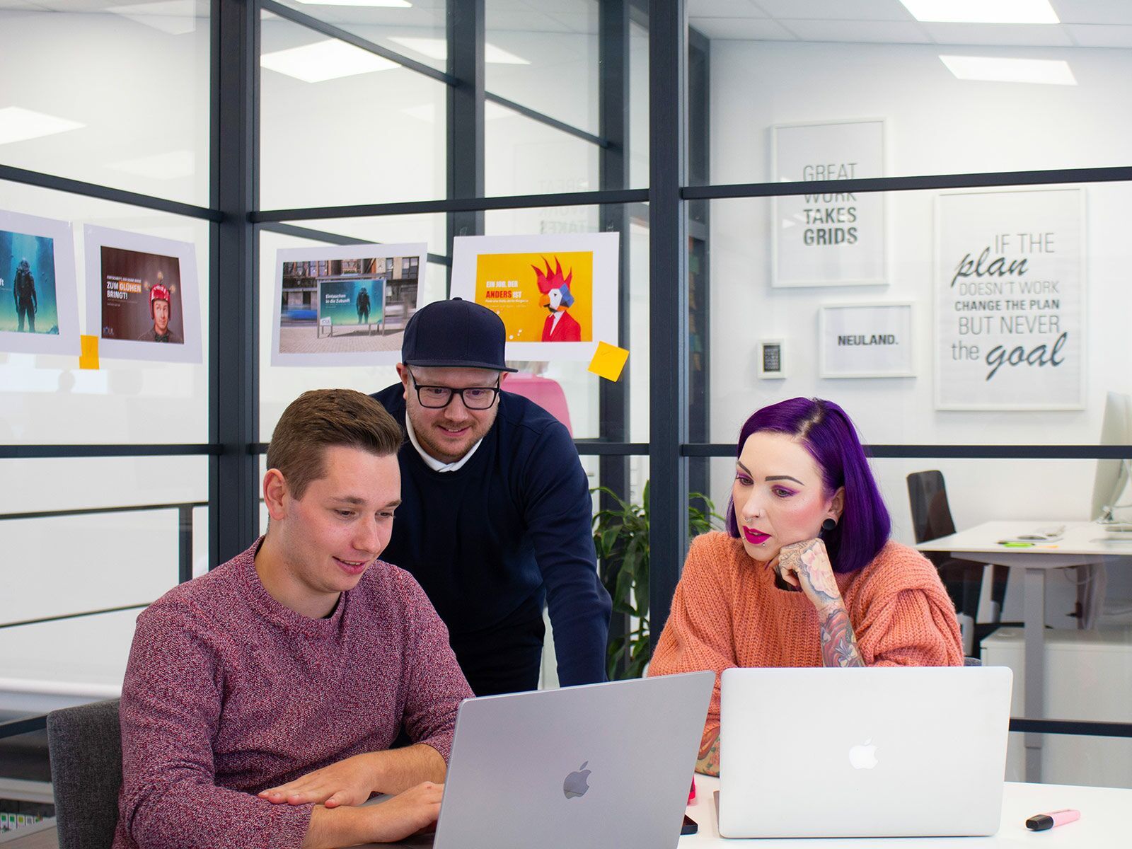 Drei Personen arbeiten in einem Besprechungsraum an Laptops.